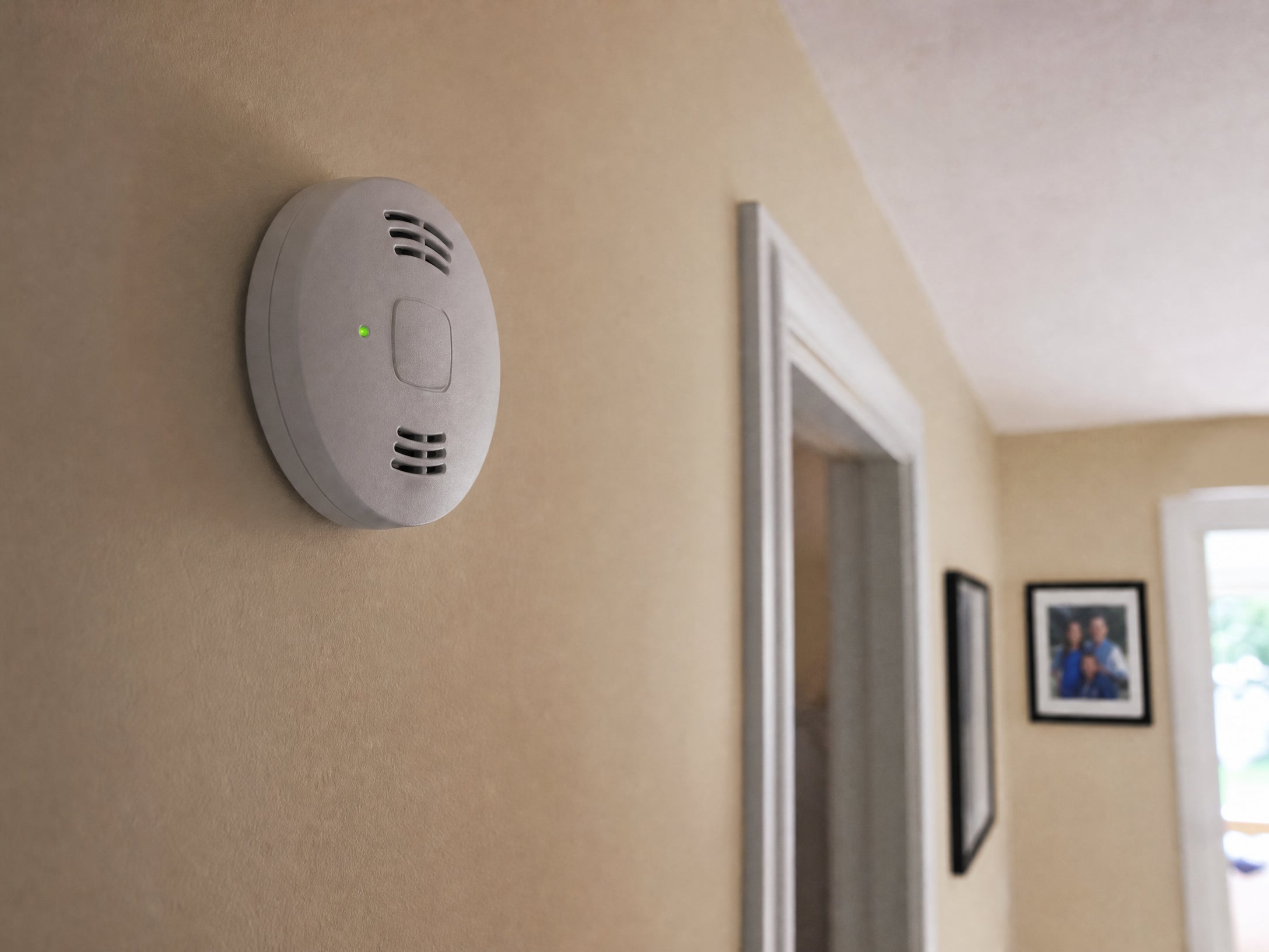 A standard carbon monoxide alarm with a green status light on a hallway wall